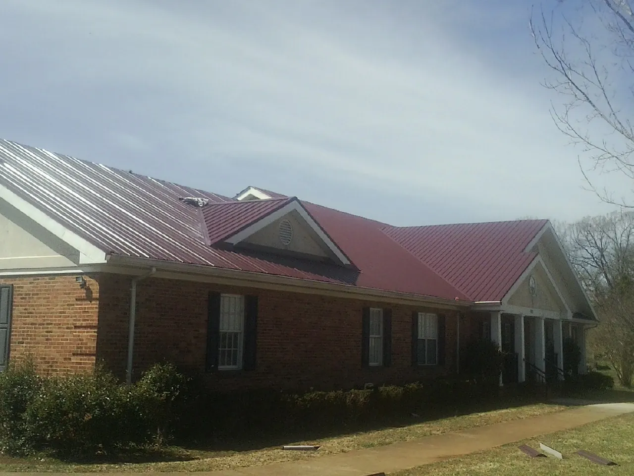 Red metal roof with gabled entries on a long brick building, from a Hail Damage Roof Repair job in Beaver Falls