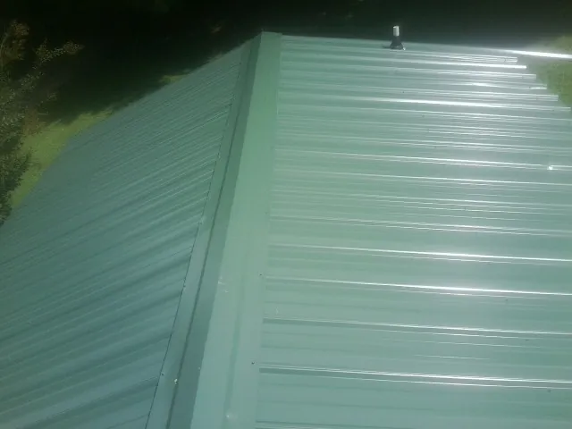 New green metal panels meeting at the ridge of a roof — Flat Roof Repair work by our crew in Beaver Falls