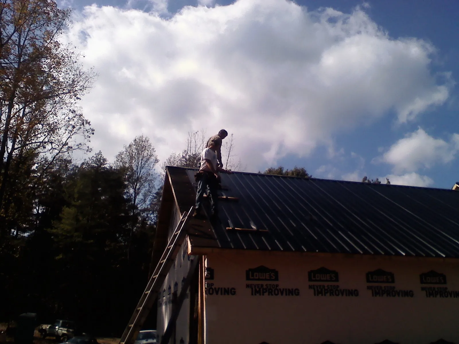 Roofer fastening dark metal panels high against a cloudy sky, from a Roof Inspection job in Beaver Falls