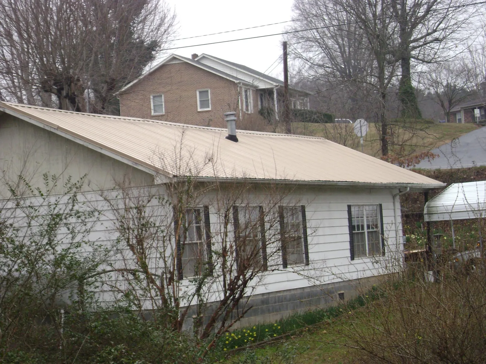 Tan metal roof on a white sided house set into a hillside — Commercial Roofing by Roofing Brothers in Beaver Falls