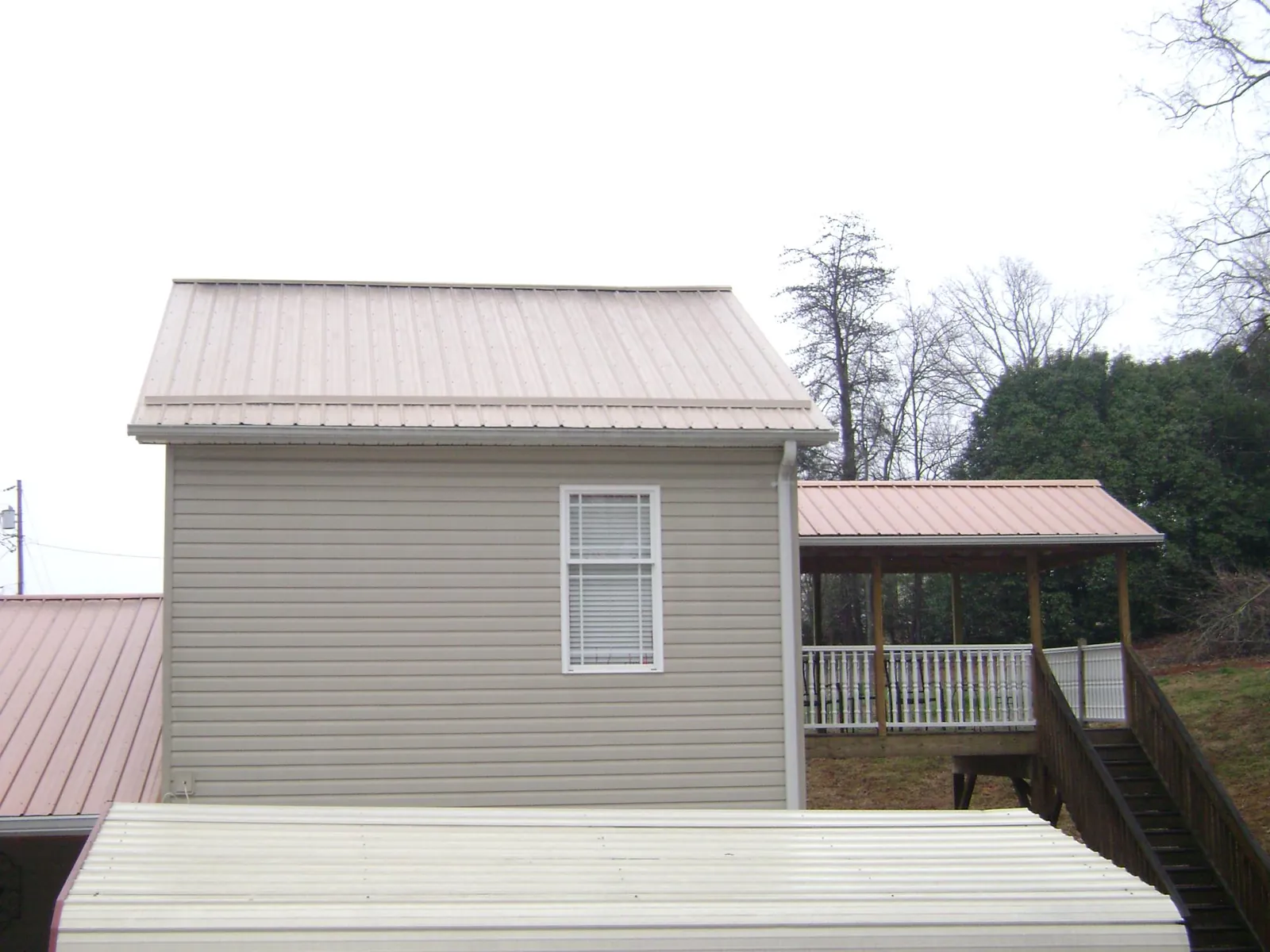 Tan metal roofs on a two story addition and attached porch, from a Roof Replacement job in Beaver Falls